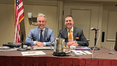 two men at table with American flag in background