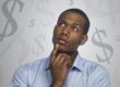 man thinking with money symbols around him.